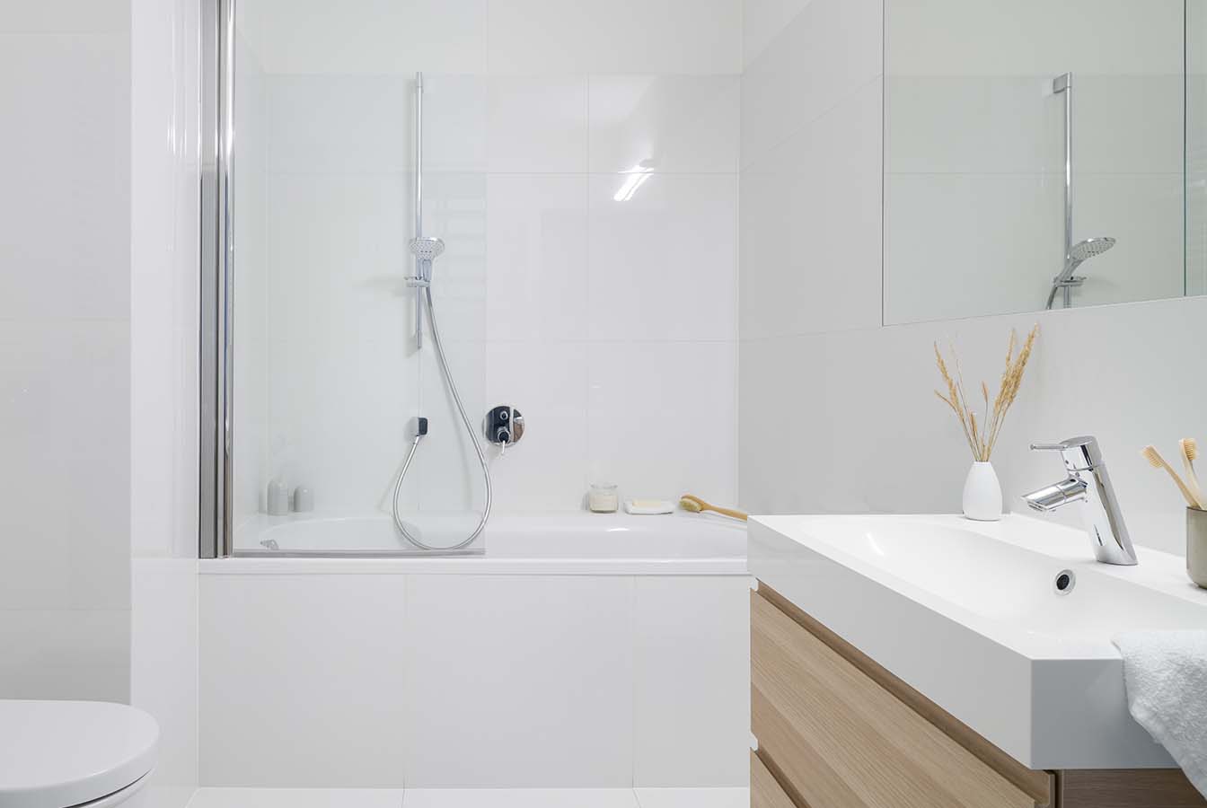 White Alcove bathtub with white shower backsplash and teak finish vanity