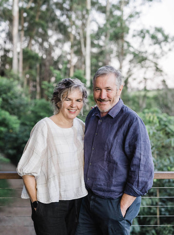 Pam and Martin Brook posing for photo on Cape Byron Distillery deck with lowland sub-tropical rainforest in the background