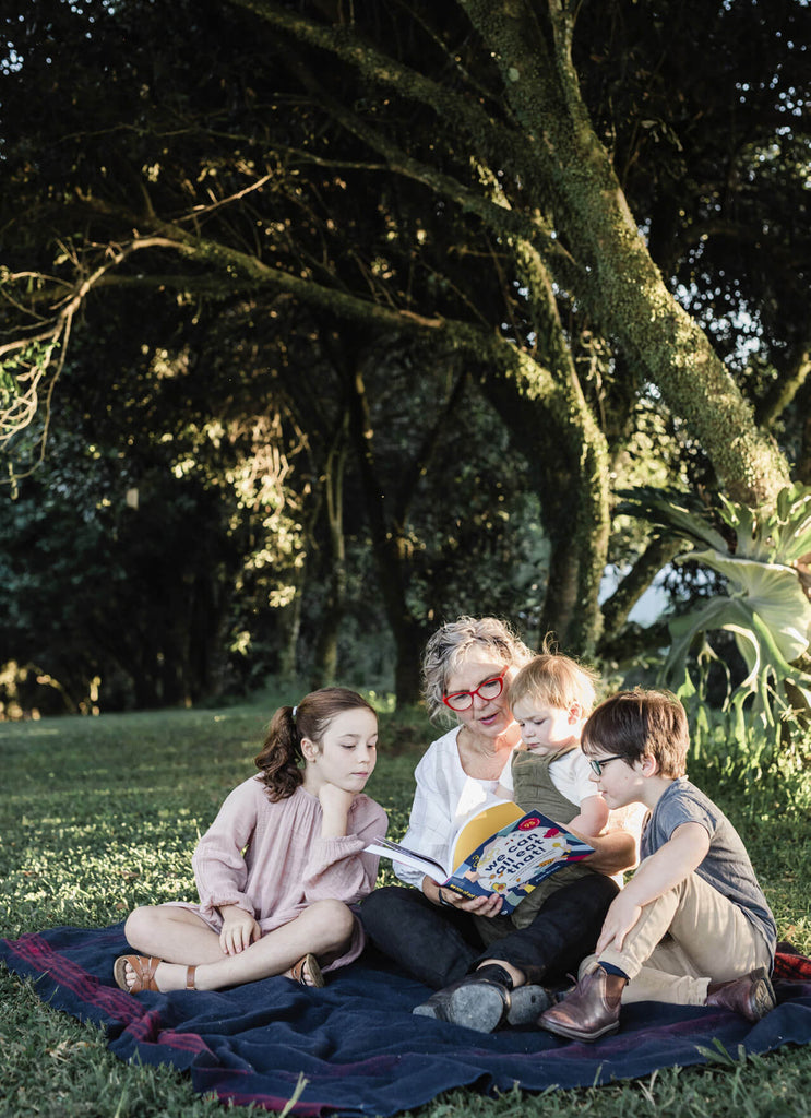 Pam Brook, co-founder of Brookfarm, sitting with her grandchildren reading We Can All Eat That in the macadamia orchard