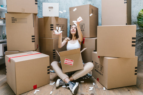 Woman sitting on floor next to cardboard boxes throwing packing peanuts into air