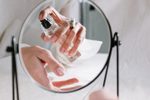 a reflection of a persons hands in the mirror applying perfume.