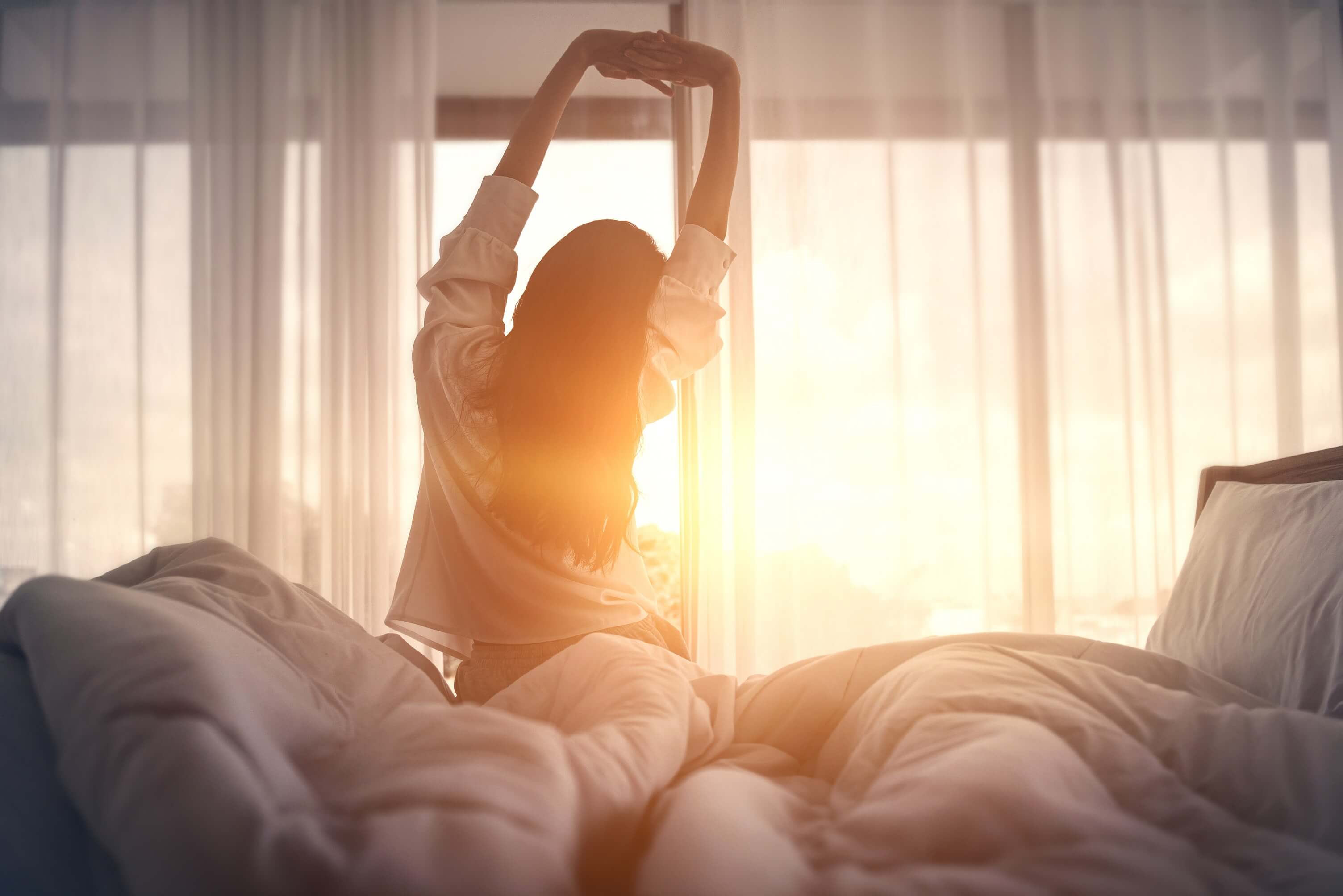 Woman stretching in the early morning in a comfortable bed after waking up from a restful night sleep.