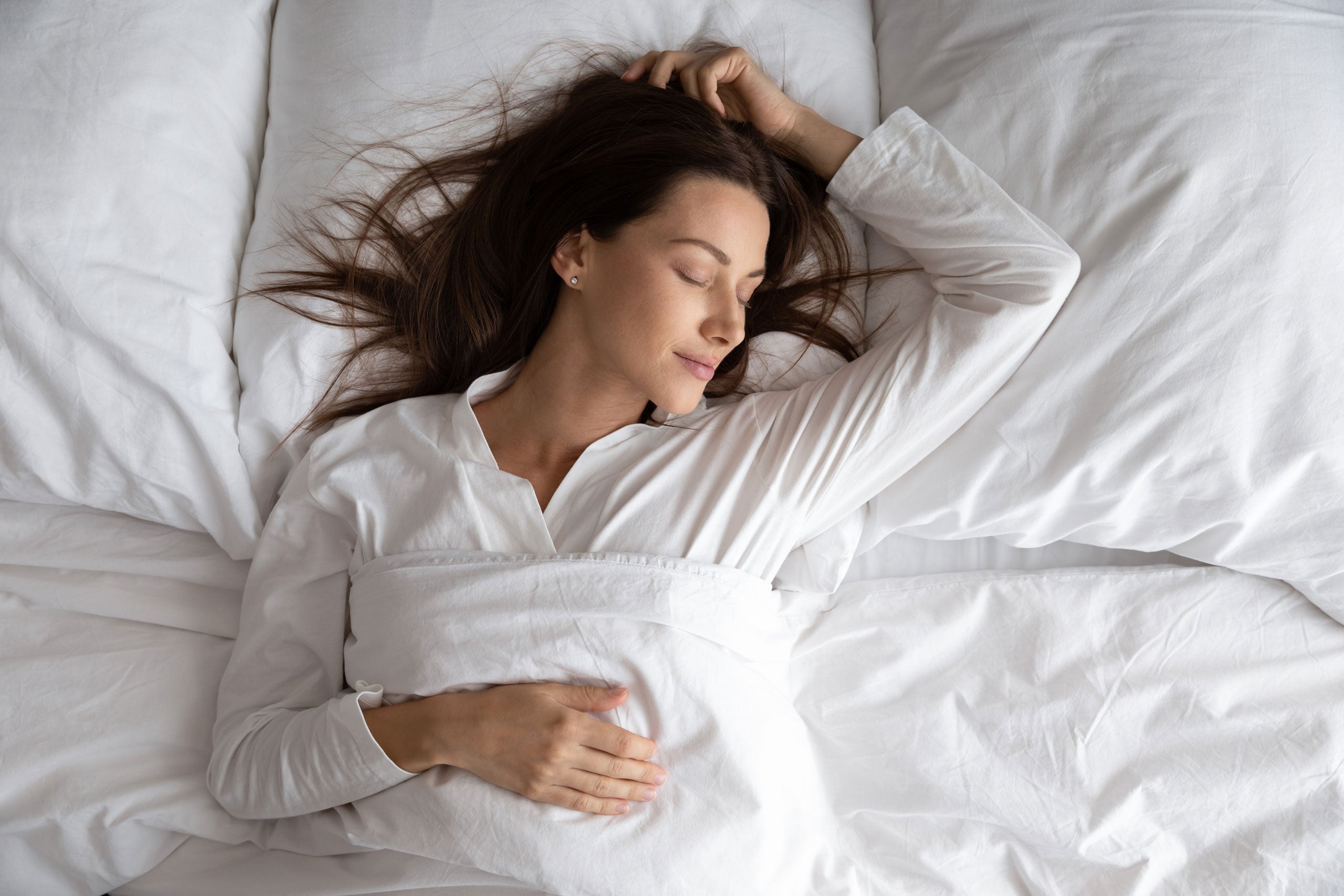 Woman lying comfortably in bed asleep with white linens.