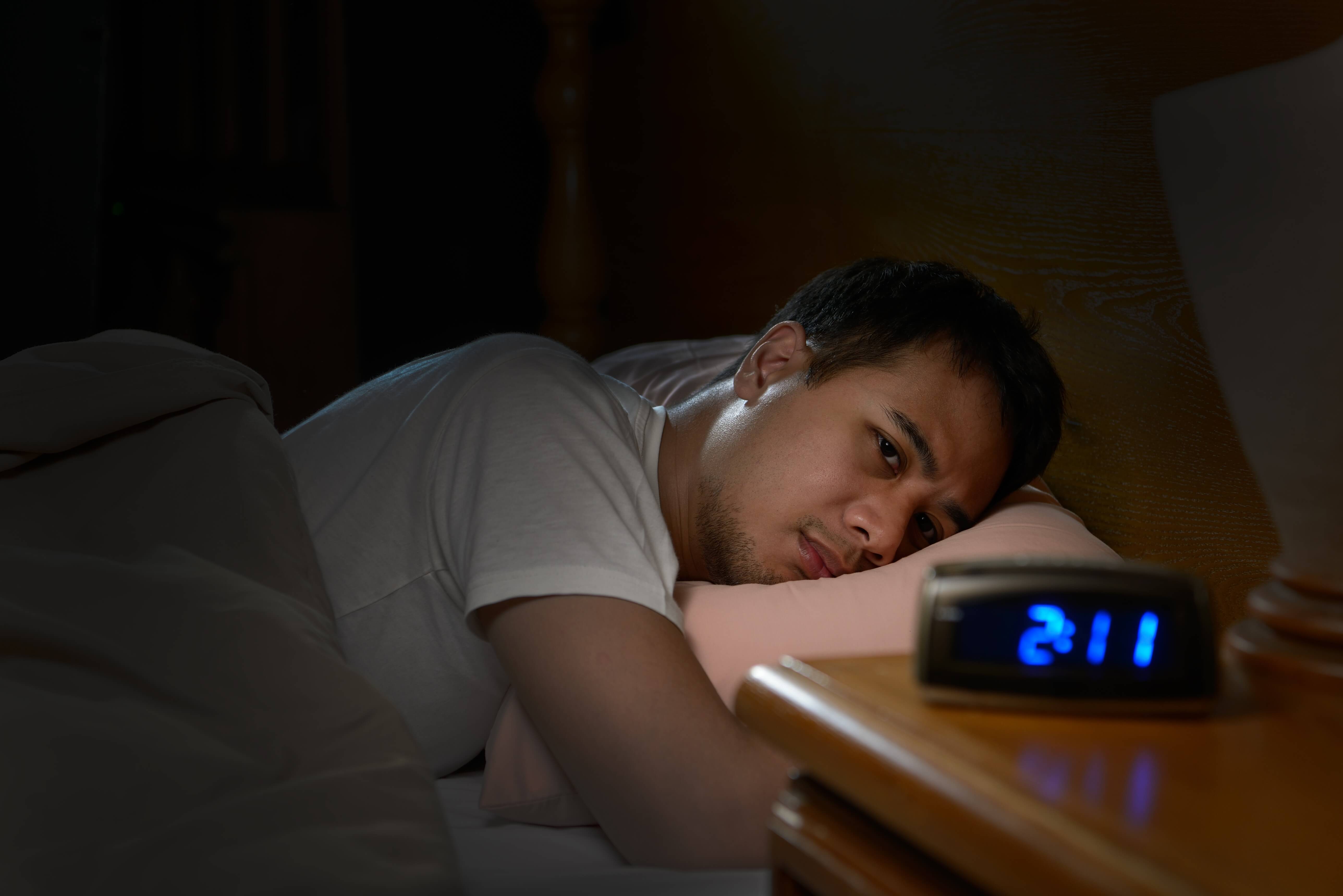 Man lying awake in bed staring at his alarm clock that says “2:11am”