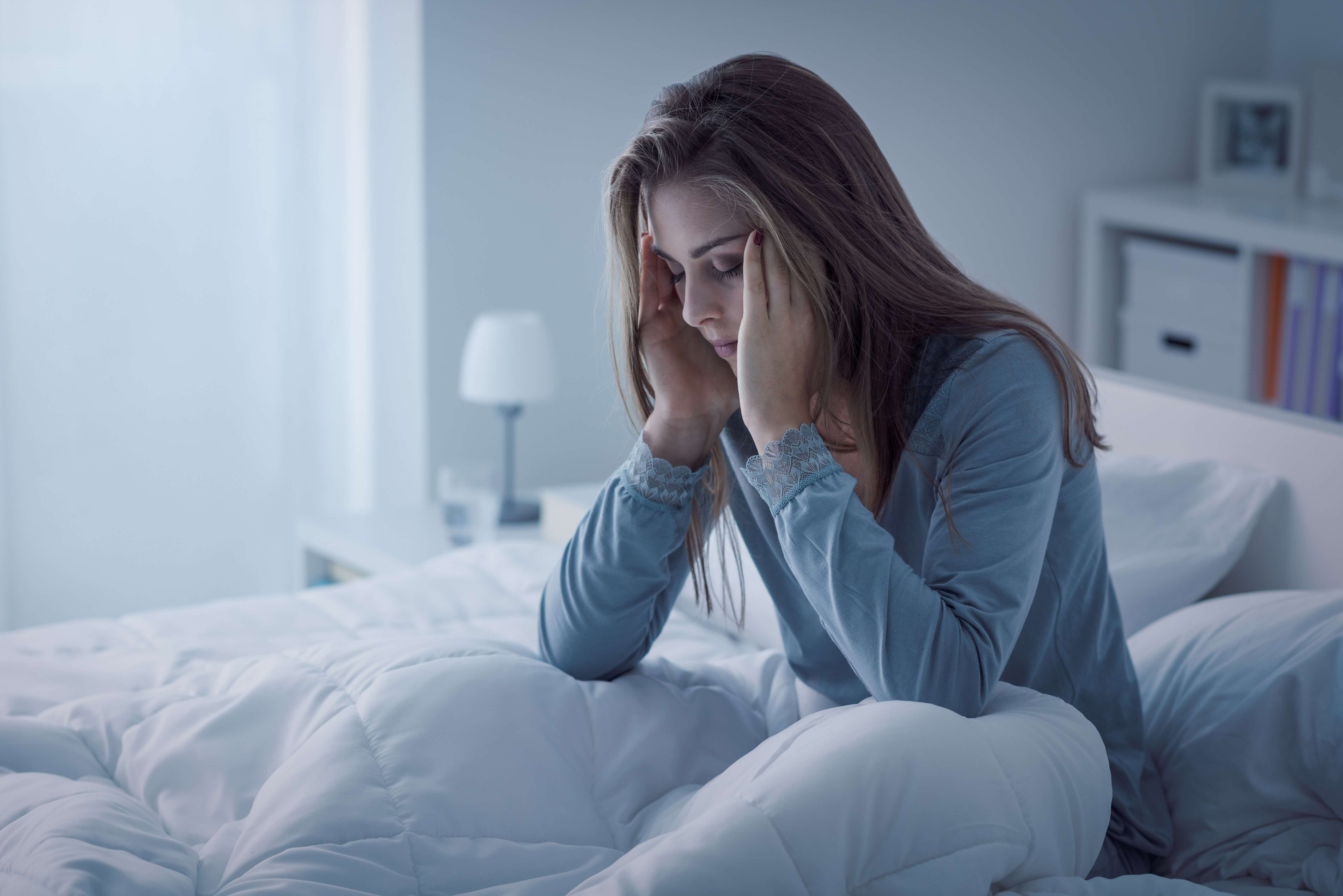 Femme assise dans un lit, se frottant les tempes, l'air stressé !