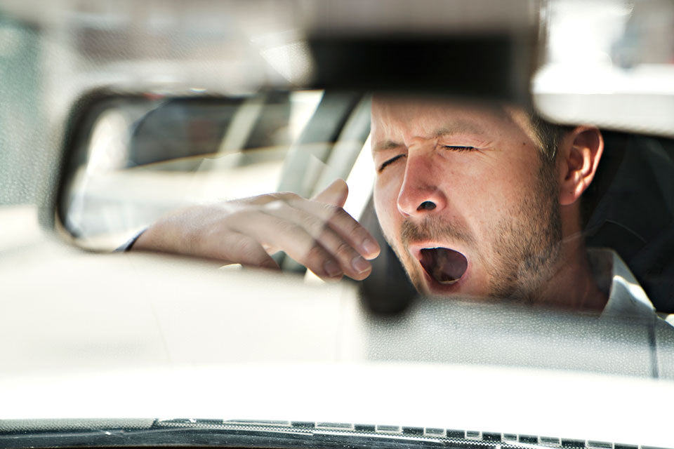 Tired man stopped at red light in car yawning from the view of the rear view mirror.