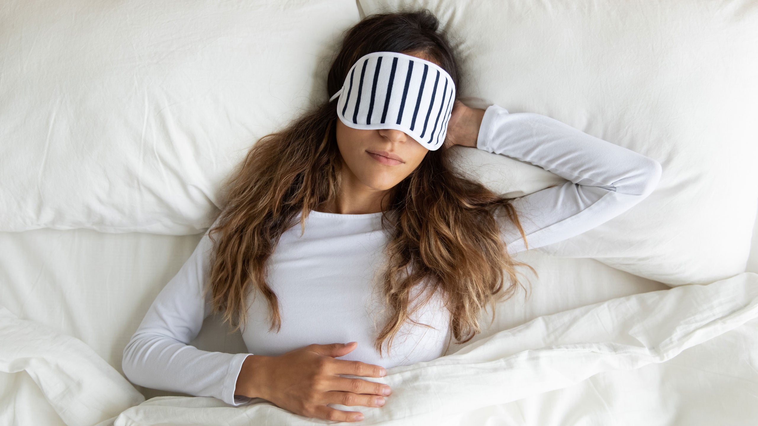 Woman lying peacefully in bed face-up with a sleep mask over her face.