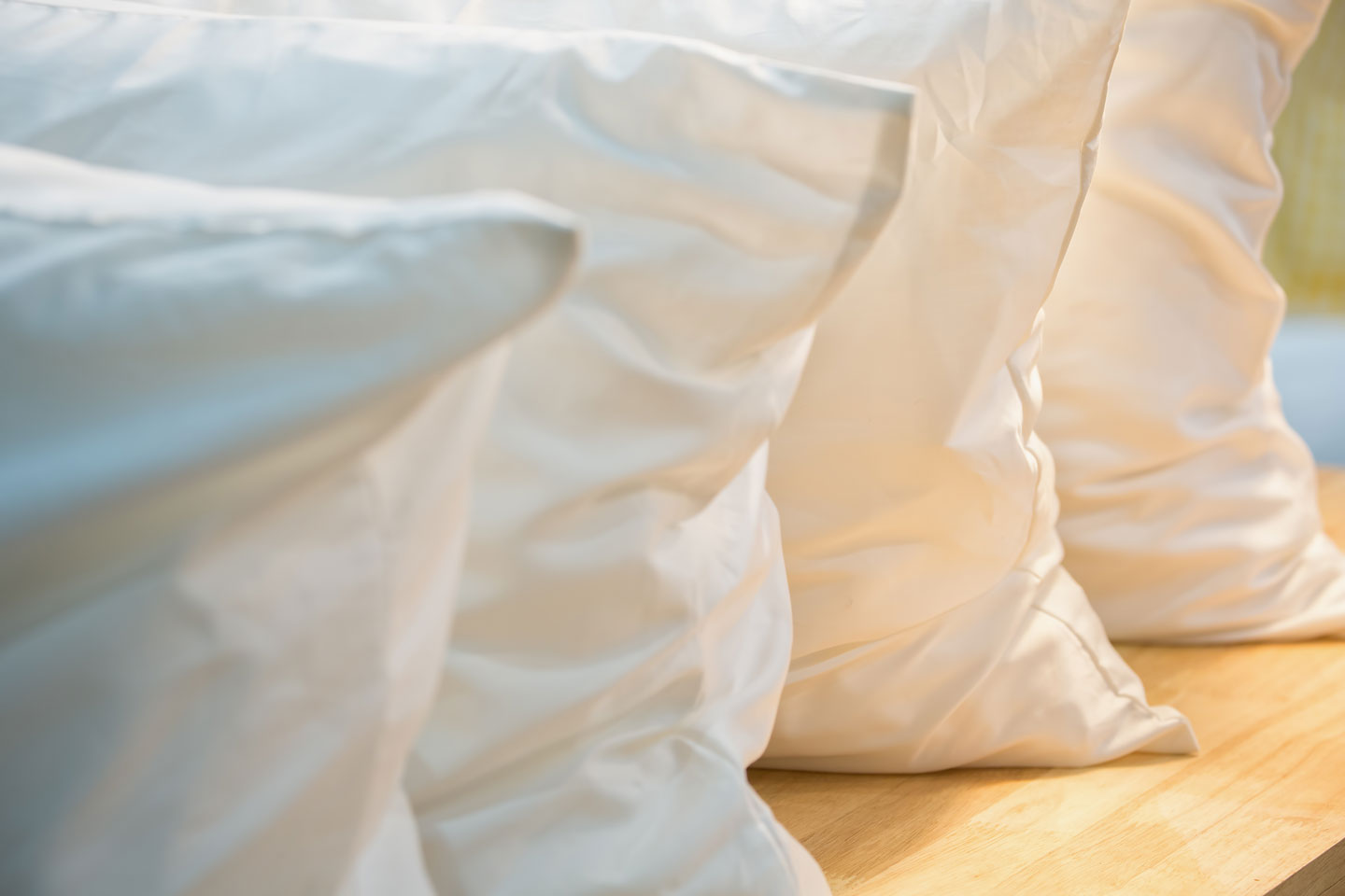 Four pillows sat up against one another on a wood board with the sunlight peeking over the pillowcases.