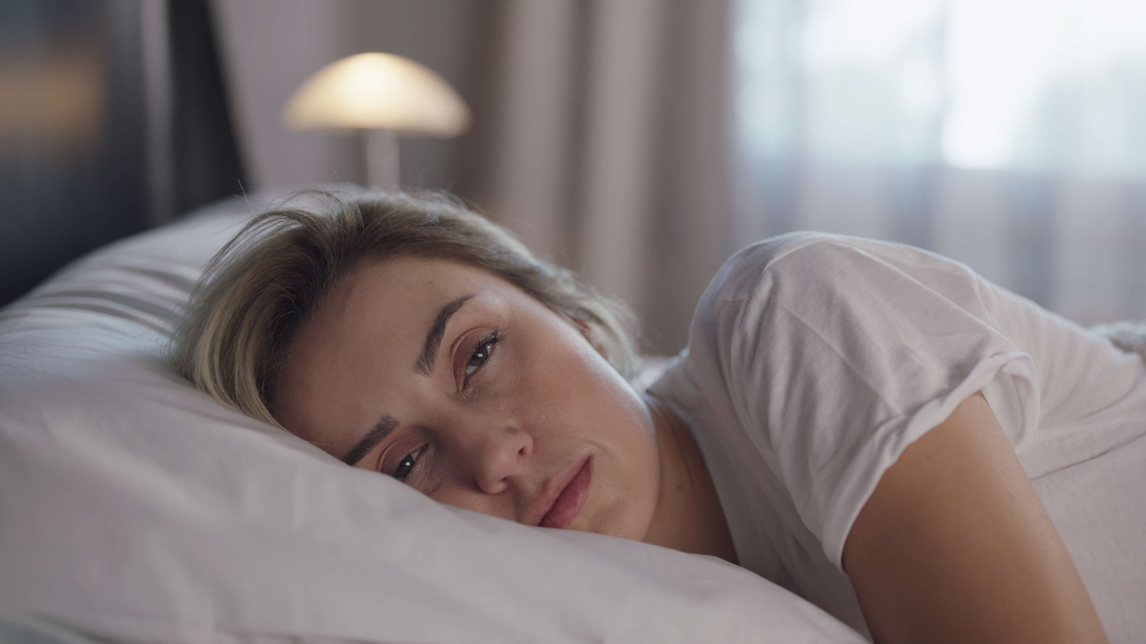 Tired woman laying in her bed staring at viewer.