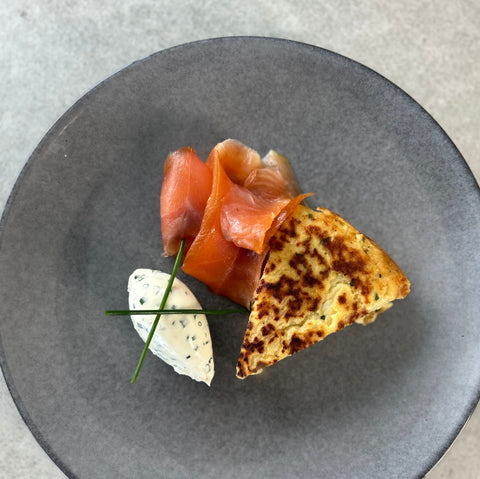 triangle of potato pancake with slices of smoked salmon and sour cream with herbs
