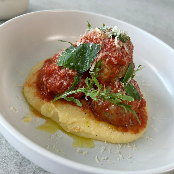 yellow polenta topped with meatballs and tomato sauce in a white bowl