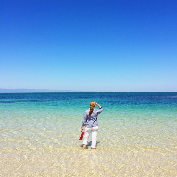 woman standing in shallow seawater looking to horizon blue skies and water