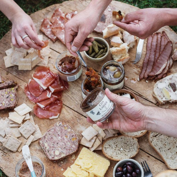 round wooden board with cured meat cheese charcuterie lots of hands in front