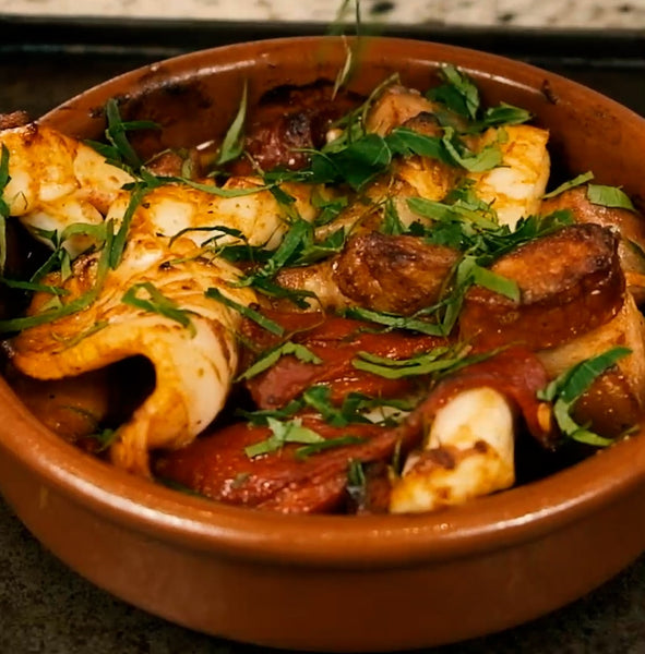 terracotta round dish with slices of squid, chorizo and pork belly