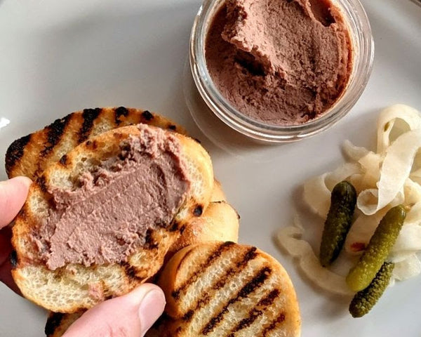open jar of pate pickles on side charred bread in hand
