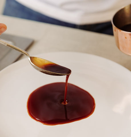 spoon with dark brown sauce pouring on to a white plate