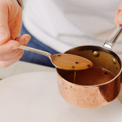 copper pan with pepper sauce being spooned onto a white plate by a person