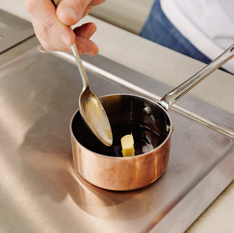 small copper pan filled with dark brown sauce which has butter being stirred in