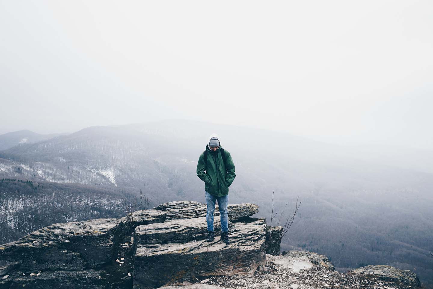 a man standing on top of a mountain with a gloomy field behind