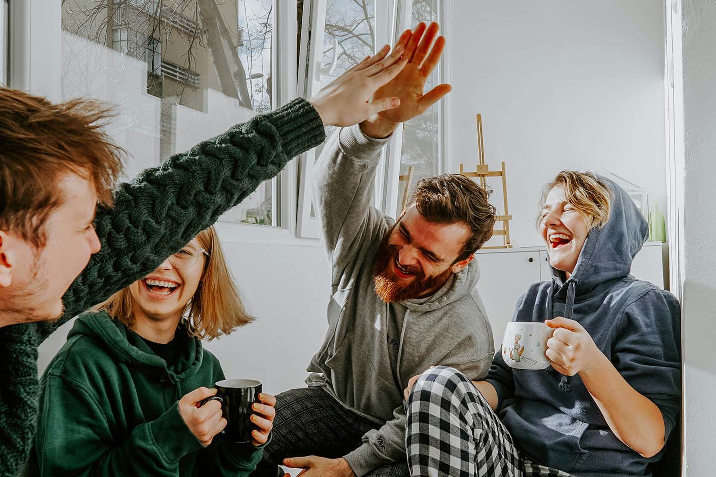 Two men high-five each other, laughing, while two women hold a cup, laughing.