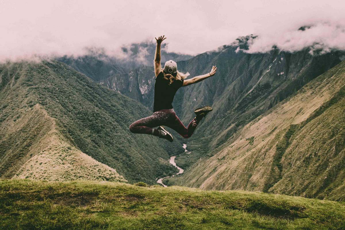 a woman leaping joyfully against a breathtaking mountain backdrop