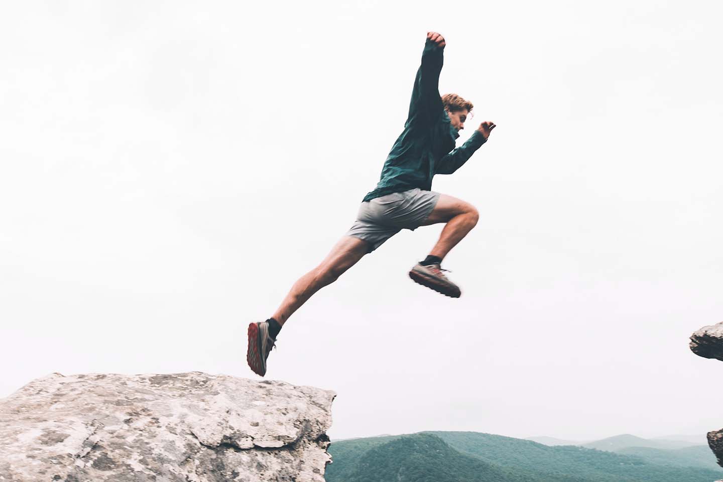 a young man jumping above rock mountain