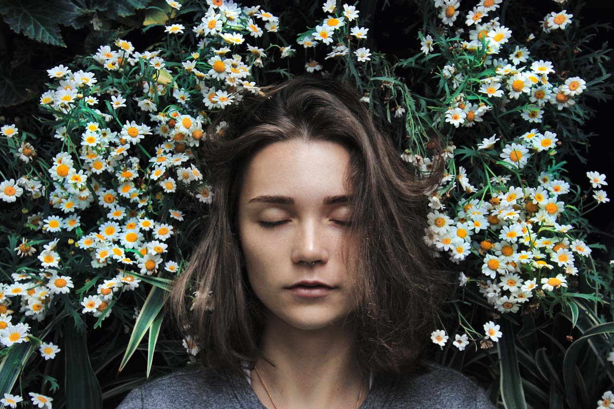 a woman with eyes closed with flowers behind her