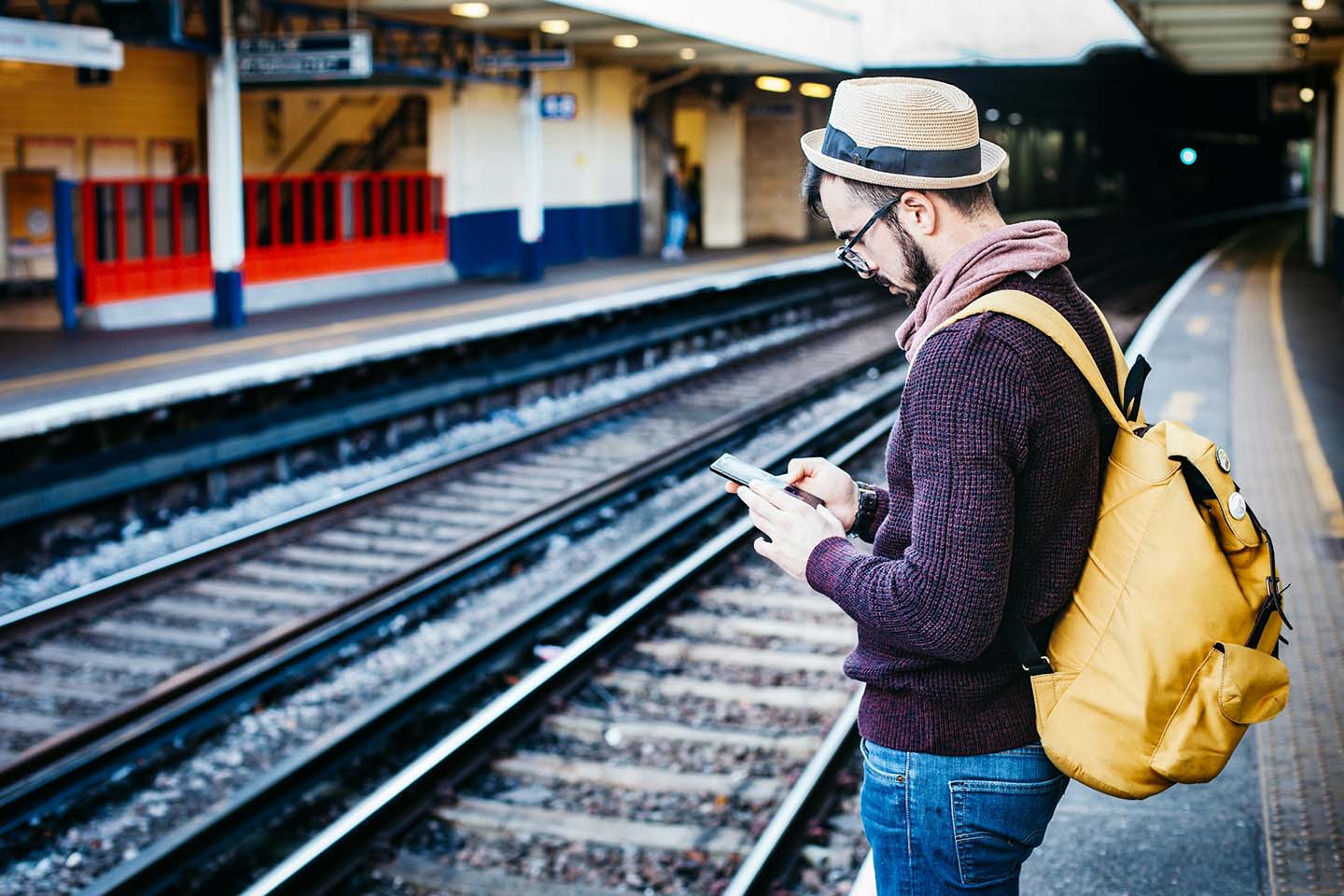 Man waiting for the train while looking at his phone at train station.
