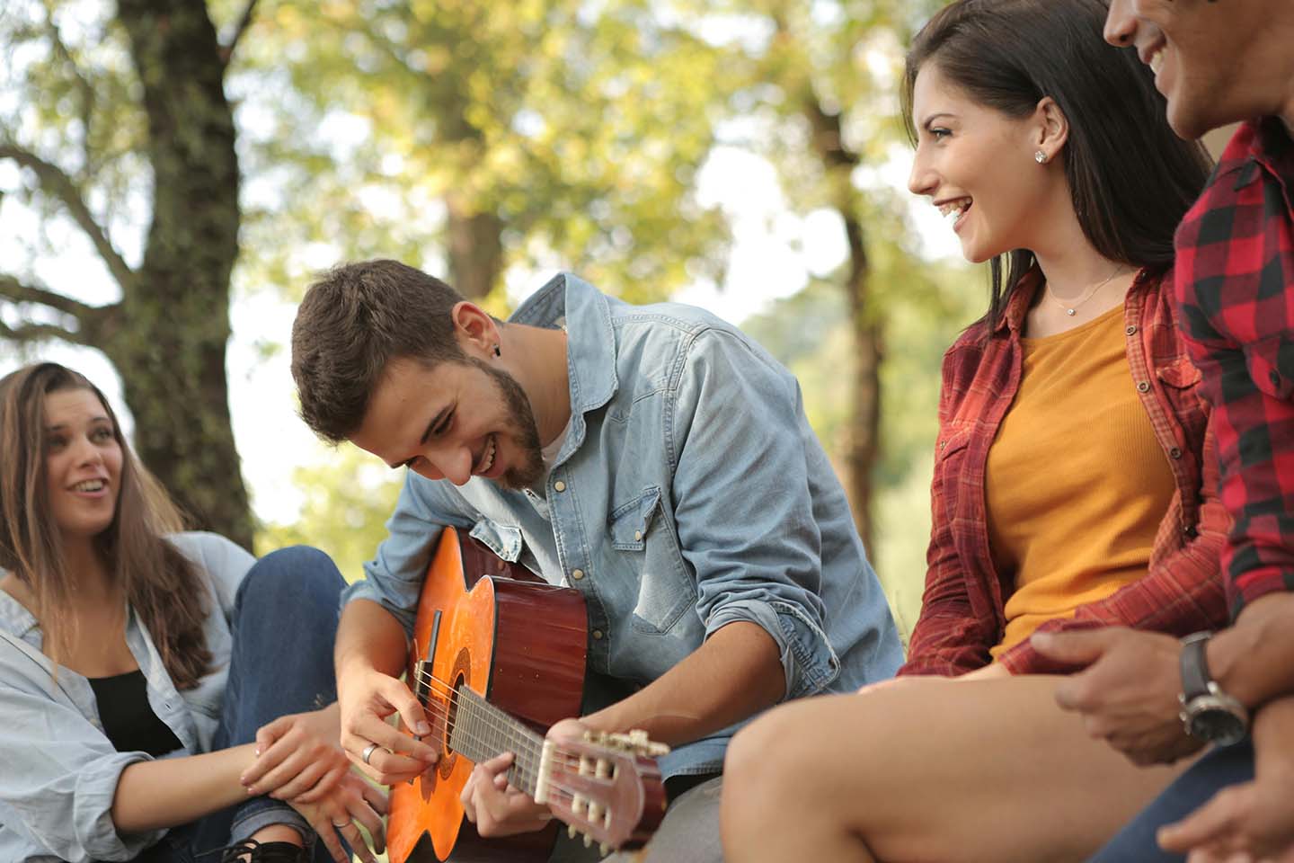 man with guitar and smiling friends sitting outside