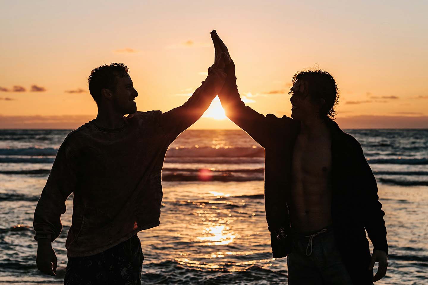 two men high-fiving on the beach at sunset