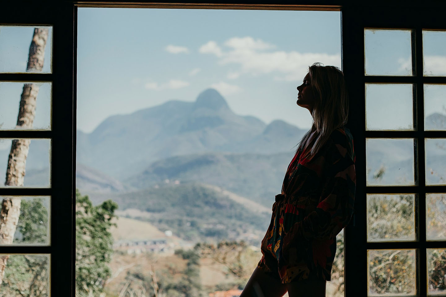 a silhouette of a woman leaning over a window looking at mountains