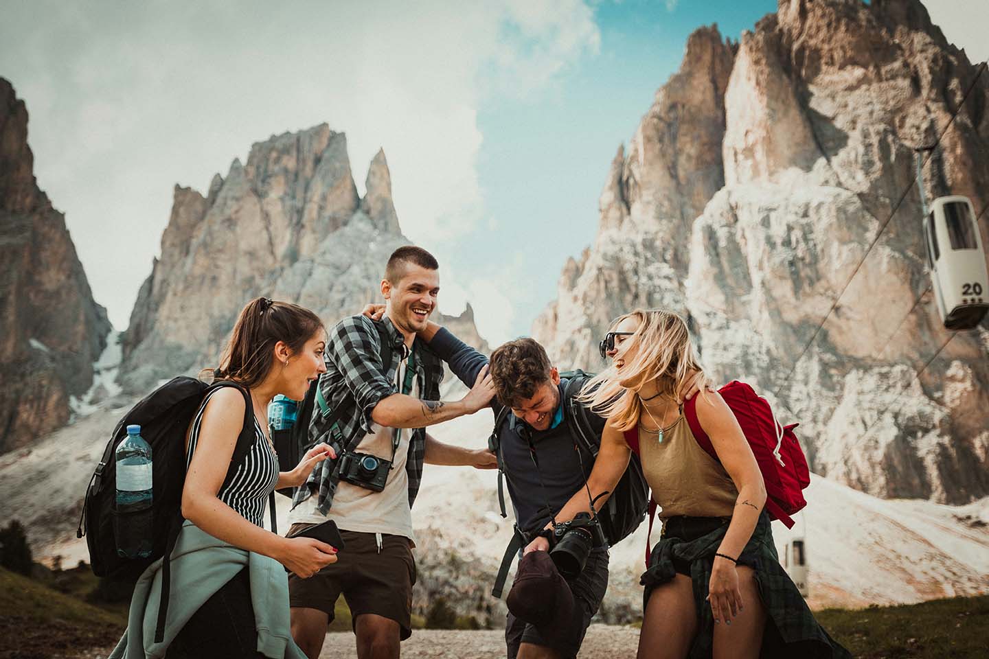 two men and two women laugh in front of a mountain range holding cameras