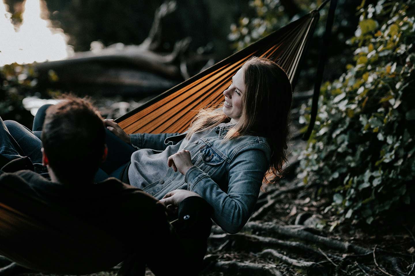 woman and man laugh in a hammock in the forest