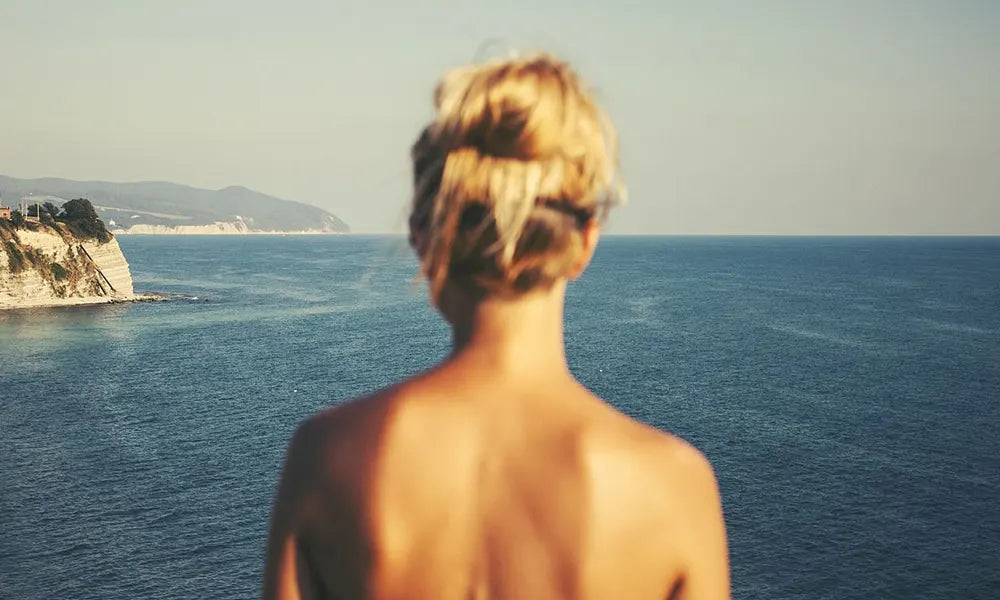 A girl looking out in the ocean from a cliff above.