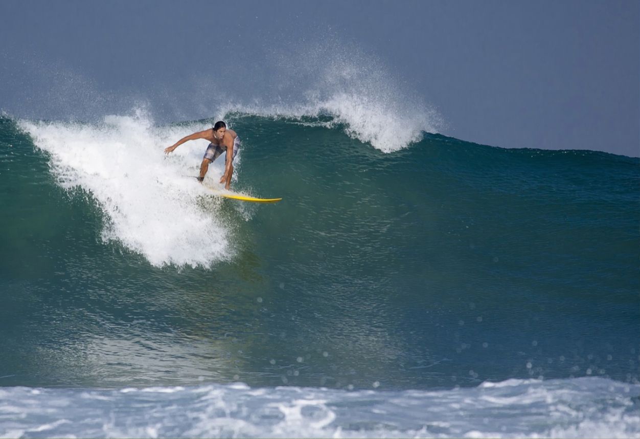 Surfista destrozando una gran ola a punto de caer. Tabla de surf amarilla y bañador gris.