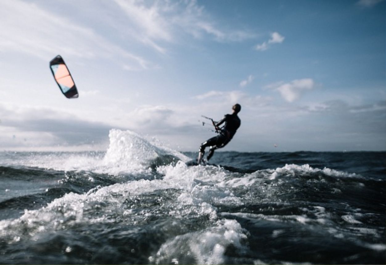 Someone wind surfing with the sail behind them and a big spray of water coming off their board.