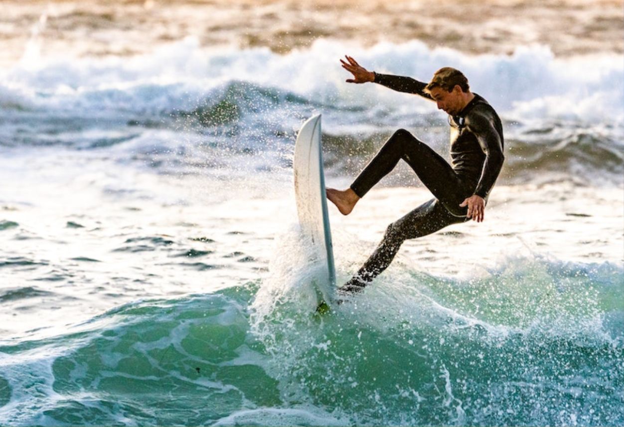 Surfista en el aire de surfear una ola con traje de neopreno completo en San Diego