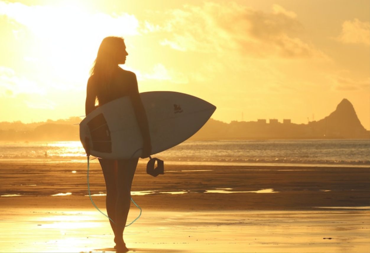 Una silueta de una niña caminando hacia el océano con una tabla de surf en la mano