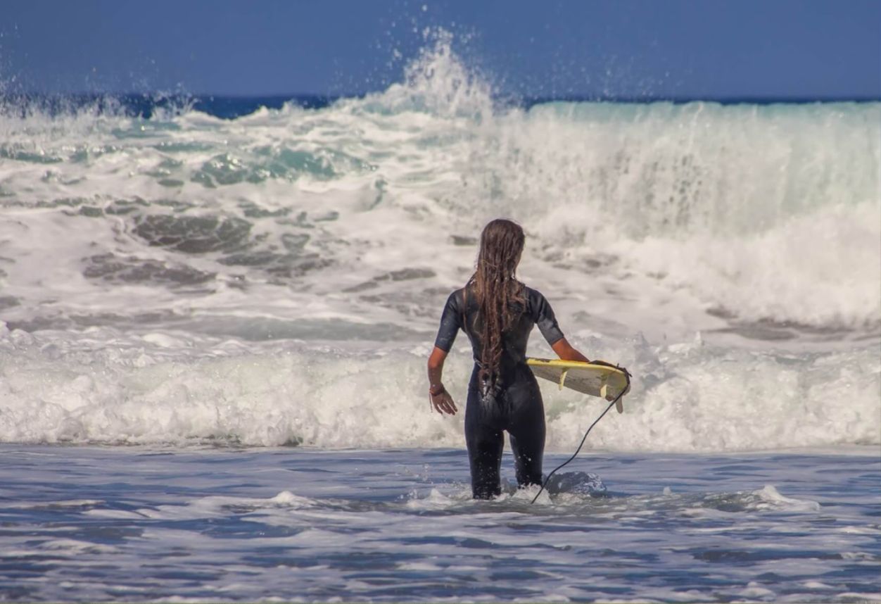 Chica con una tabla de surf a punto de adentrarse en aguas bravas para surfear con su tabla de surf