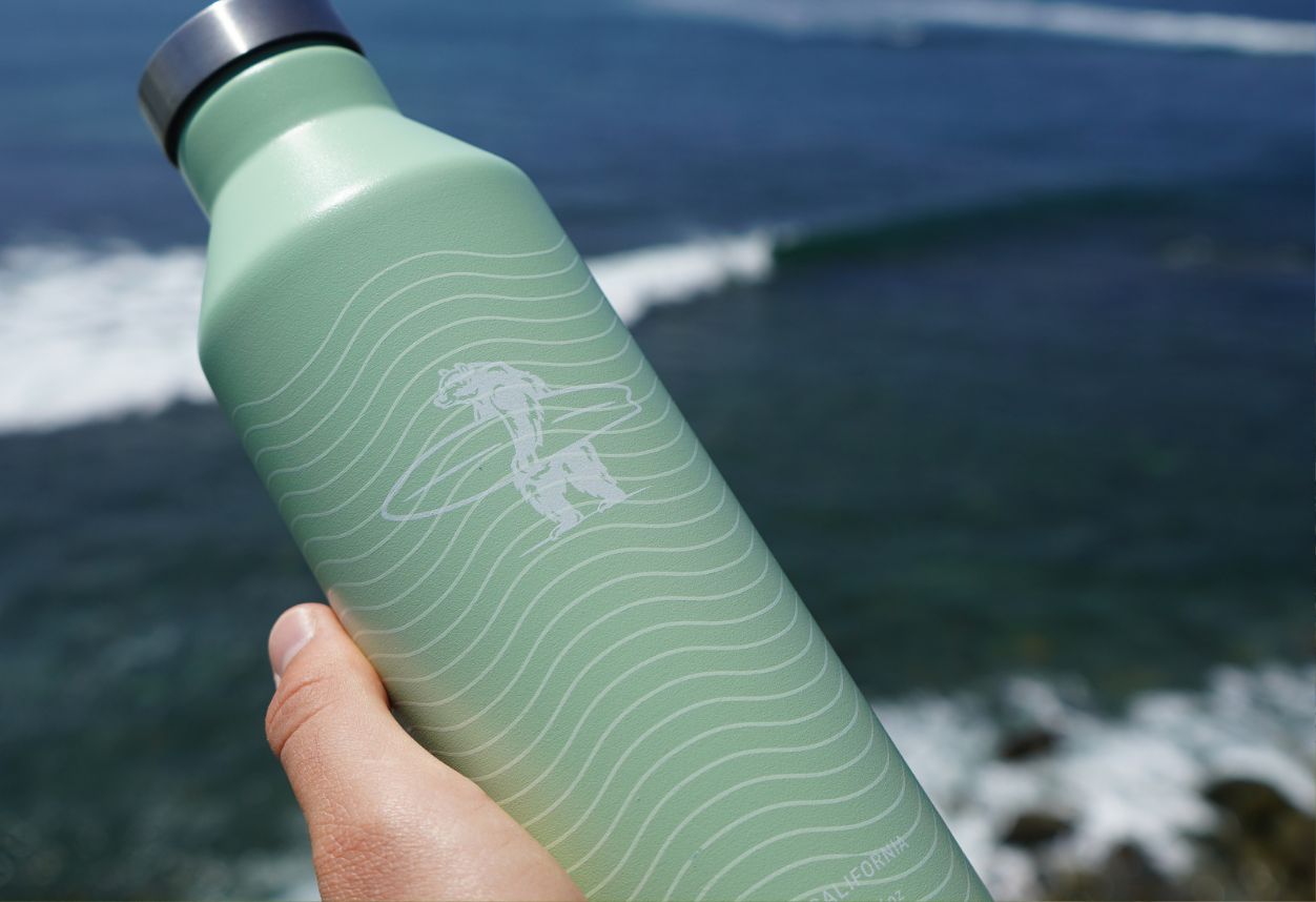 Mint green water bottle in front of the ocean waves