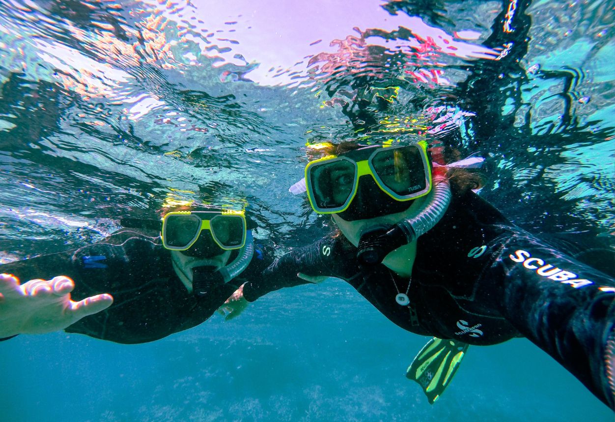 two snorkelers underwater looking at the camera with neon underwater masks