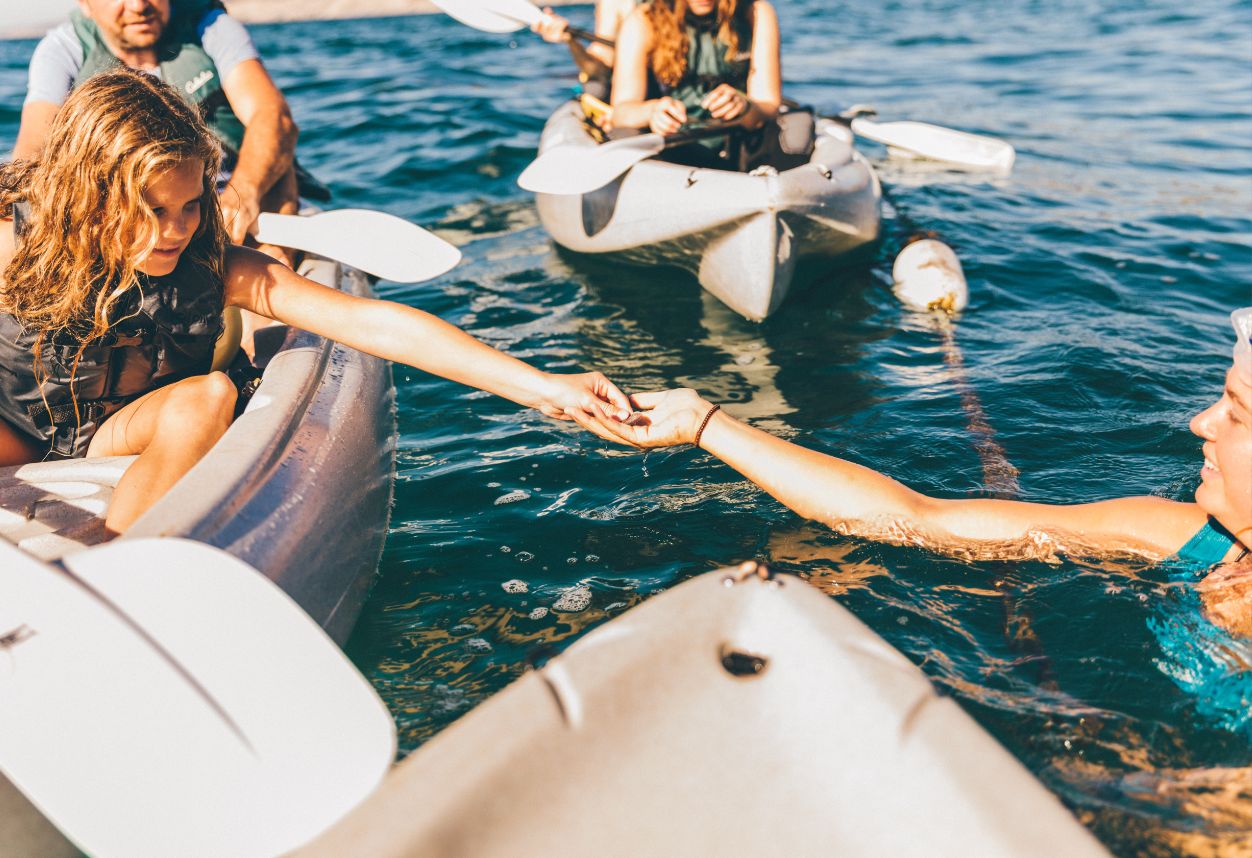 A tour guide handing a kid in a kayak a live sandollar