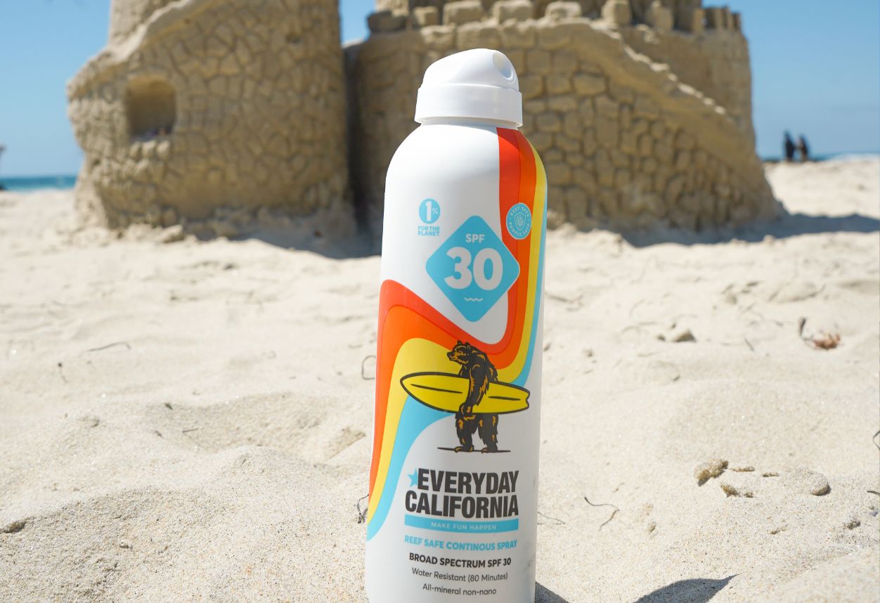 A bottle of reef safe sunscreen on the sand in front of an impressive big sandcastle.