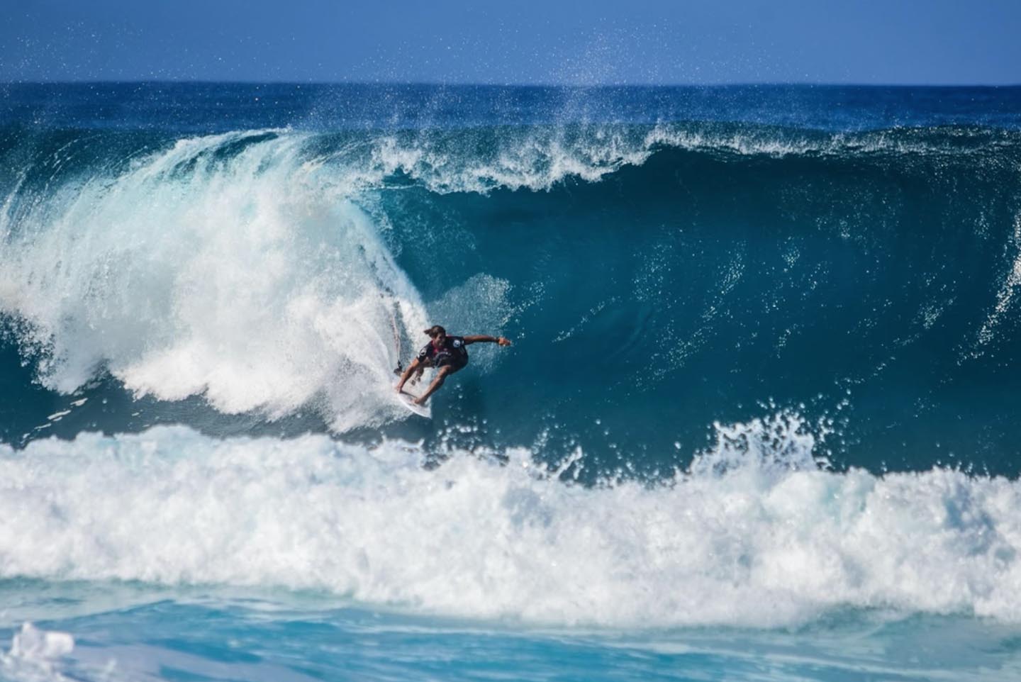 Sufer in the ocean on a sunny day surfing through the center of a large wave.