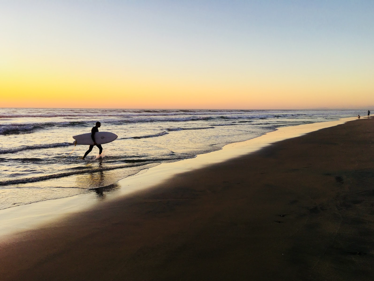 Una foto de la playa de La Jolla Shores. El sol se pone en el horizonte y hay una persona que emerge de las tranquilas aguas de las costas de La Jolla.
