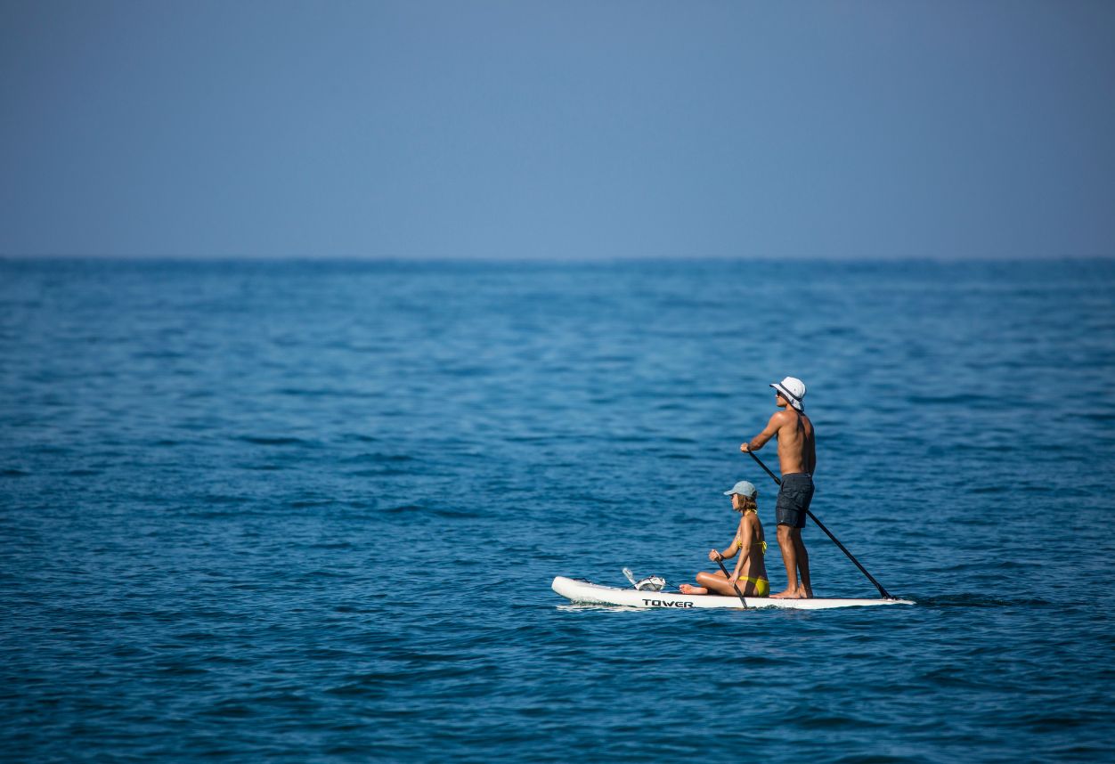 A couple on an inflatable paddle board on the Pacific Ocean seeing the san Diego coastline renting from Everyday California