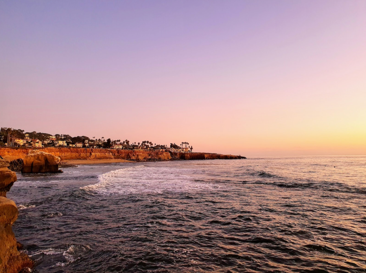 Bonita puesta de sol sobre las olas y acantilados de San Diego. Cielo morado y amarillo con agua azul oscuro y acantilados arenosos.