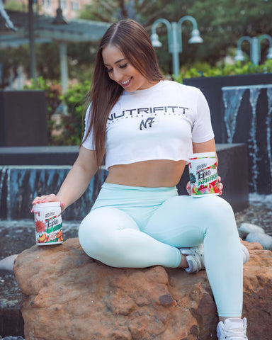 A woman smiling with two tubs of NutriFitt pre-workout.