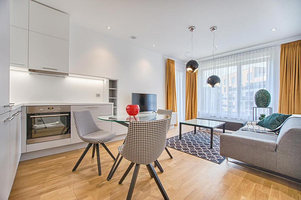 modern living room and kitchen with small glass top dining table, couch, tv, and window with blinds