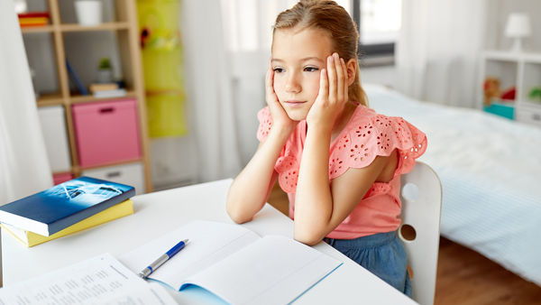 young girl sitting at a desk with her chin in her hands and a sad look on her face